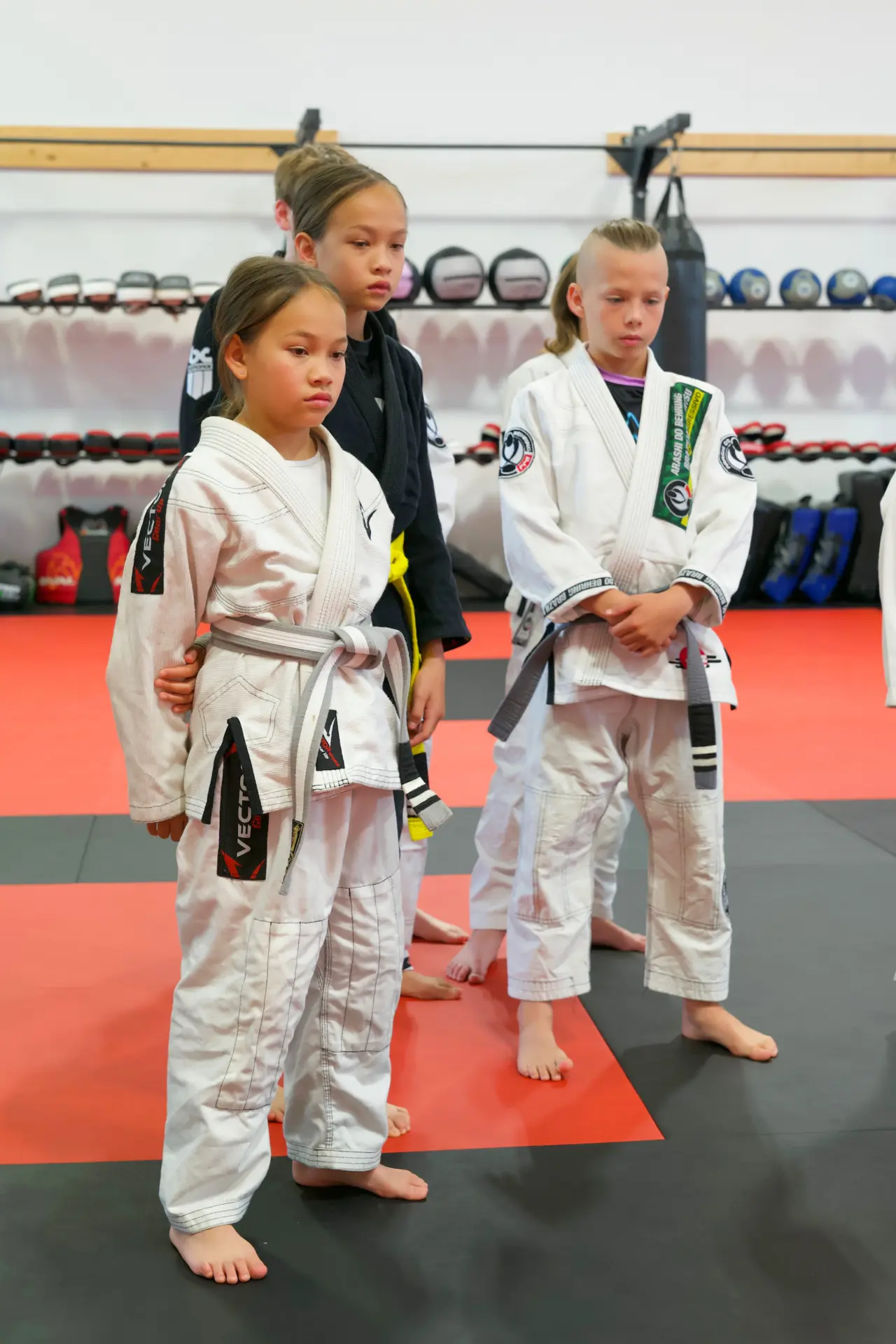 Junior Brazilian Jiu Jitsu students in white and black gis standing at attention in line before class at Arashi-Do Red Deer