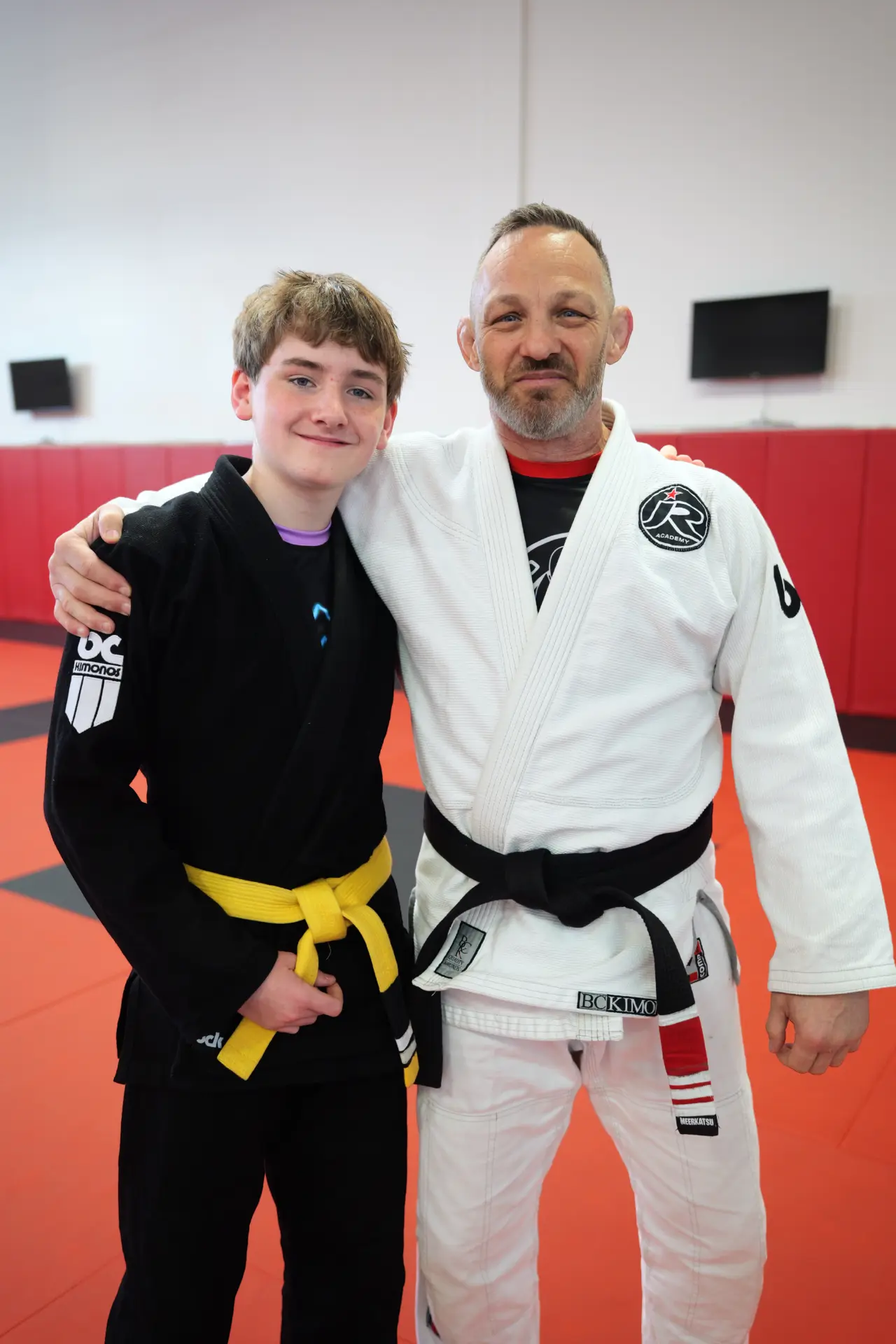 Instructor in a white gi and black belt with his arm around a teenage student in a black gi and yellow belt at Arashi-Do Red Deer
